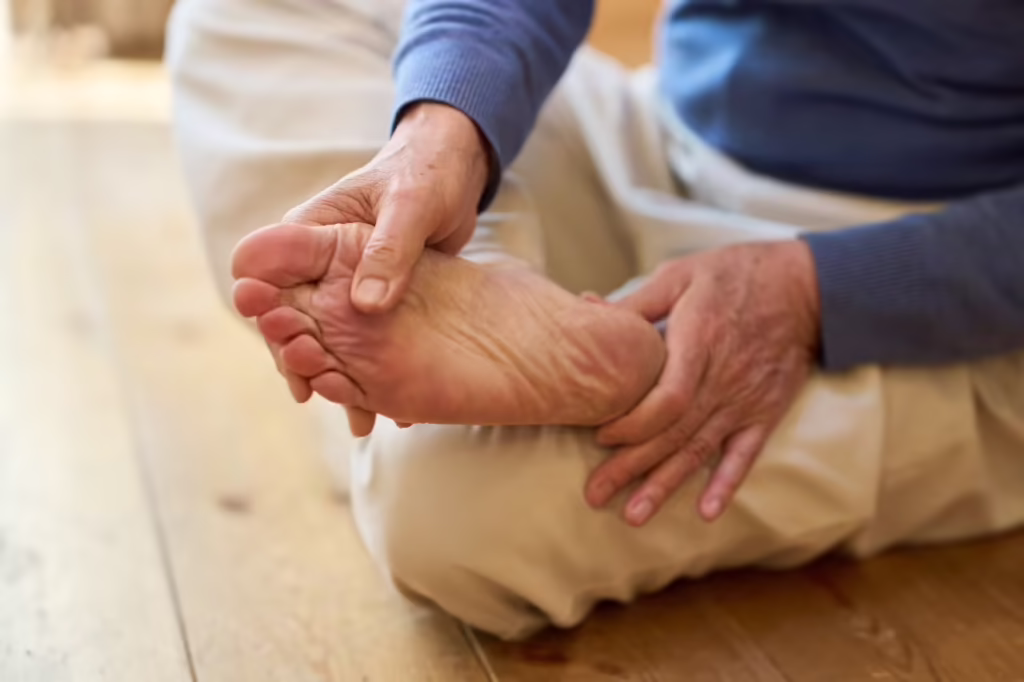 A senior Asian man touching the sole of his foot to indicate localized foot pain.
